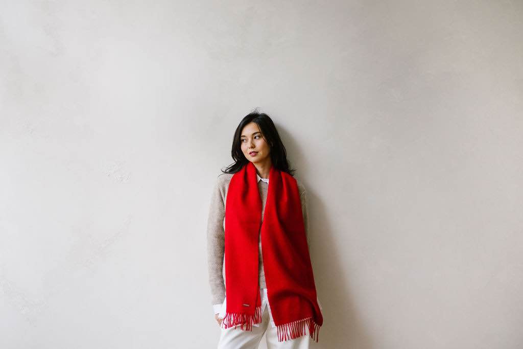 Woman standing and wearing a warm red BellePaga Baby Alpaca scarf. An elegant, soft and naturally warm piece, perfect for enhancing a winter outfit.